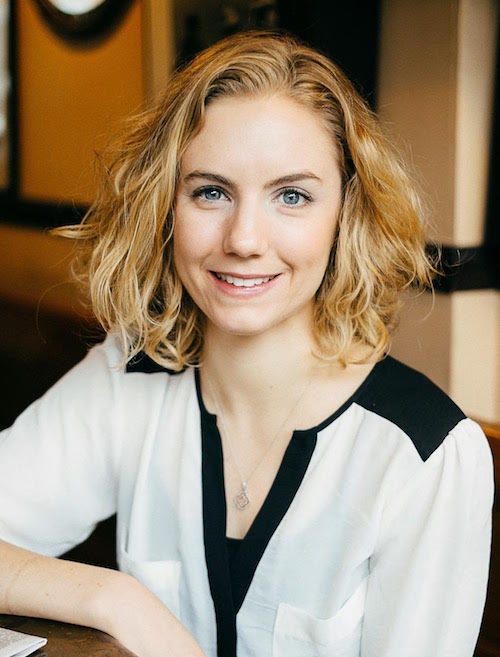 Clare's headshot. Her blonde wavy hair frames her face and she wears and white and black blouse